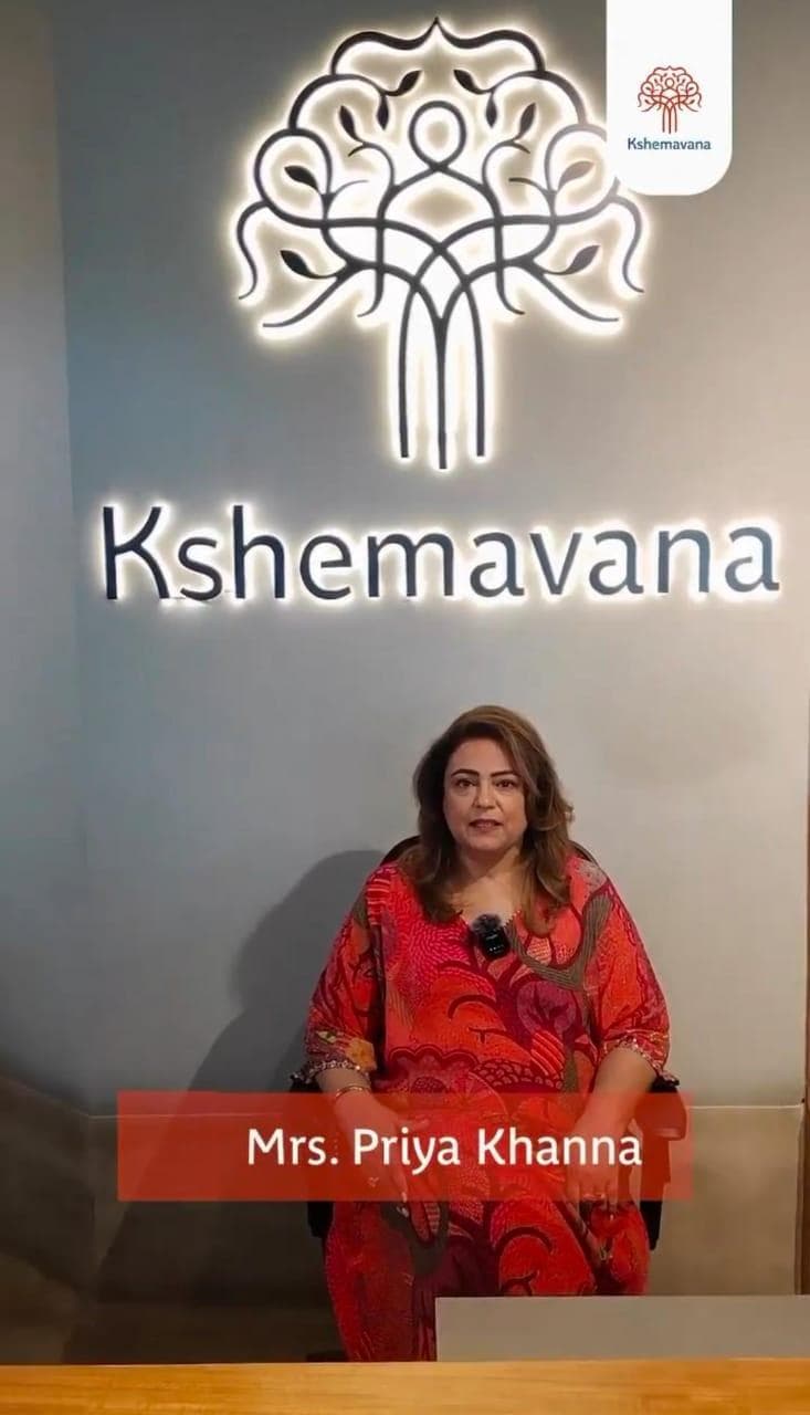 Testimonial video still: Mrs. Priya Khanna in front of the illuminated Kshemavana logo